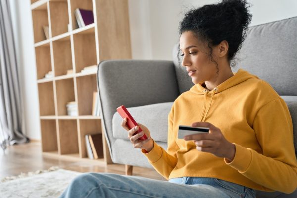 young-adult-african-american-girl-sitting-indoors-doing-mobile-payment-online--e1686043869600.jpg