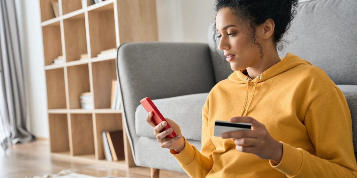 young-adult-african-american-girl-sitting-indoors-doing-mobile-payment-online--e1686043869600.jpg